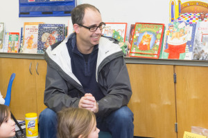 Adult volunteer laughing with kids in classroom with many picture books.